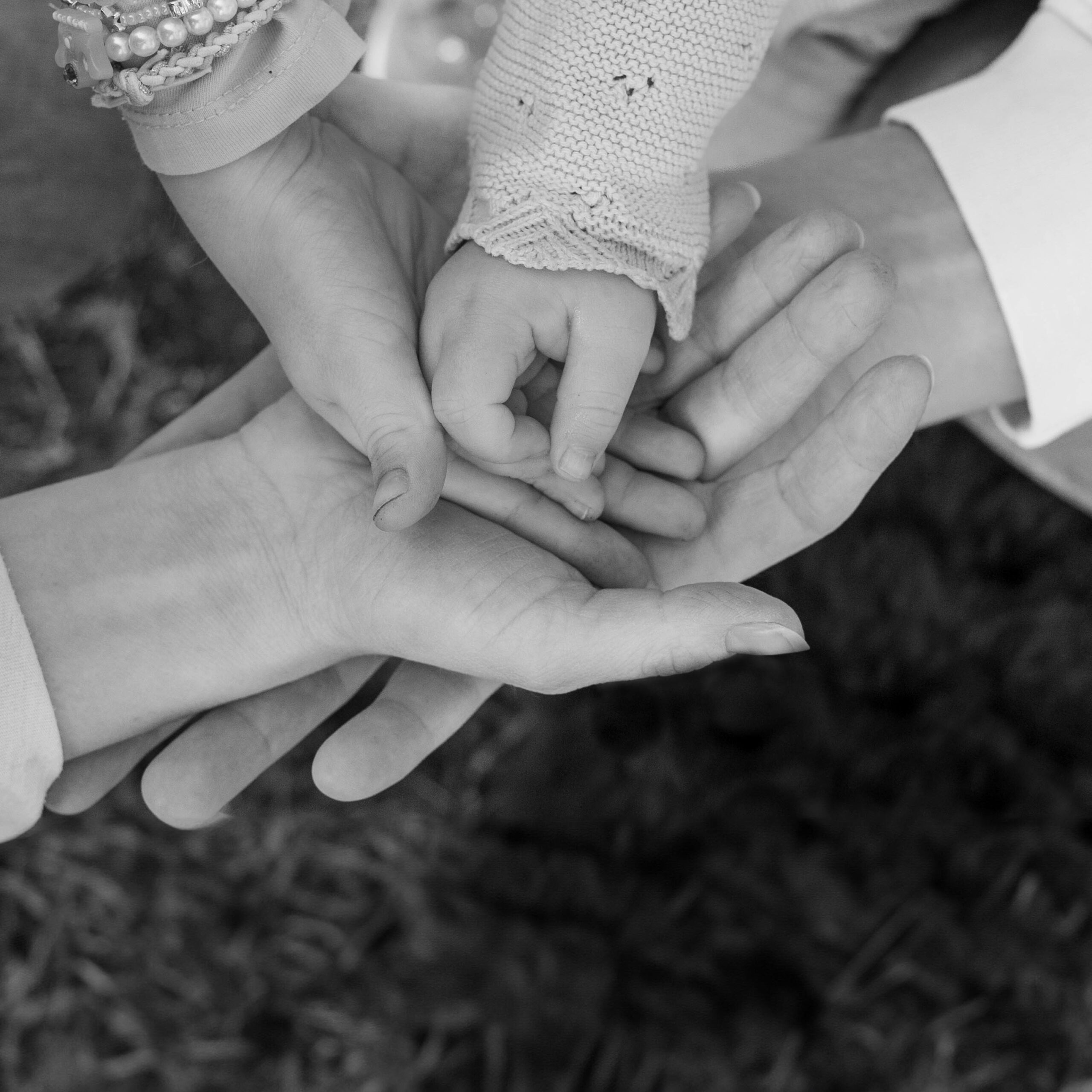 Alle Hände einer vierköpfigen Familie liegen übereinander. Foto ist in schwarz/weiß.
